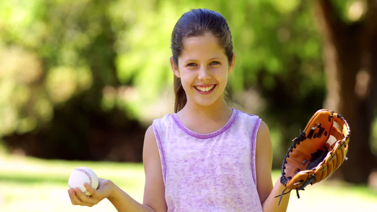 niña deportiva sonriendo a la cámara en el parque jugando con el béisbol