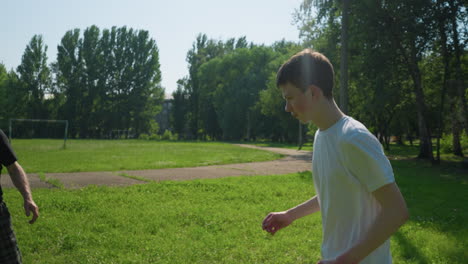 a young boy runs across a grassy field, full of energy, while his grandfather stands near by, with a goalpost in the background