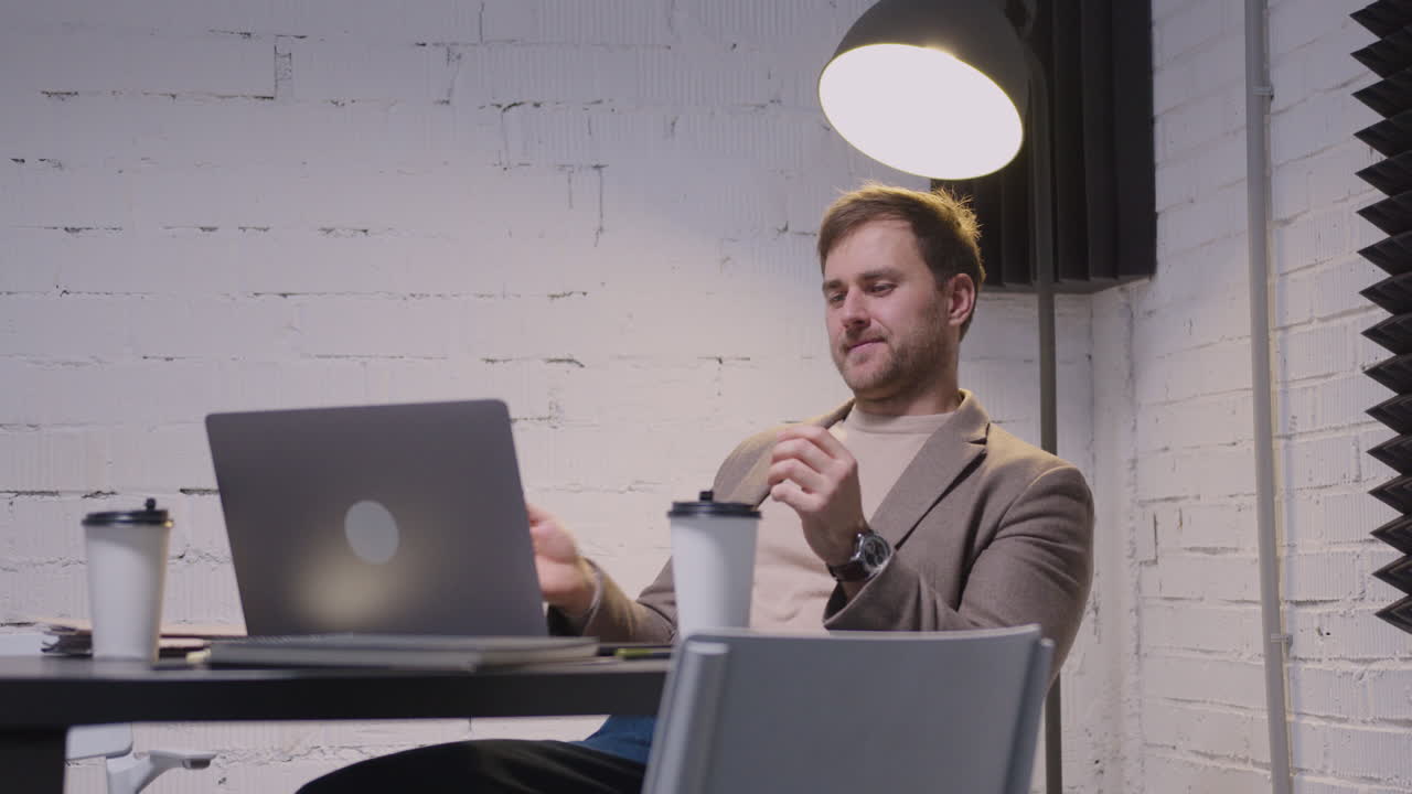 Serious Businessman Playing With A Tennis Ball And Looking At Laptop Computer While Sitting At Table In The Boardroom