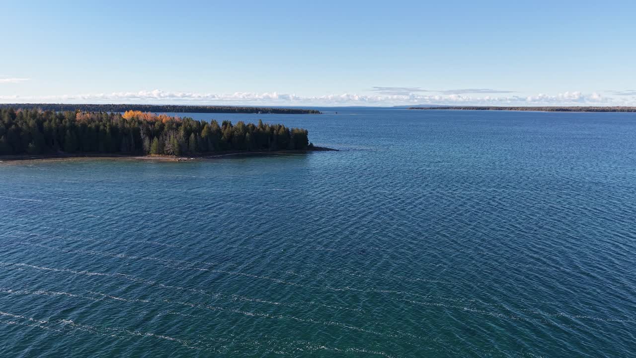 Crisp aerial view over deep blue Lake Superior with a distant wooded shoreline under clear skies