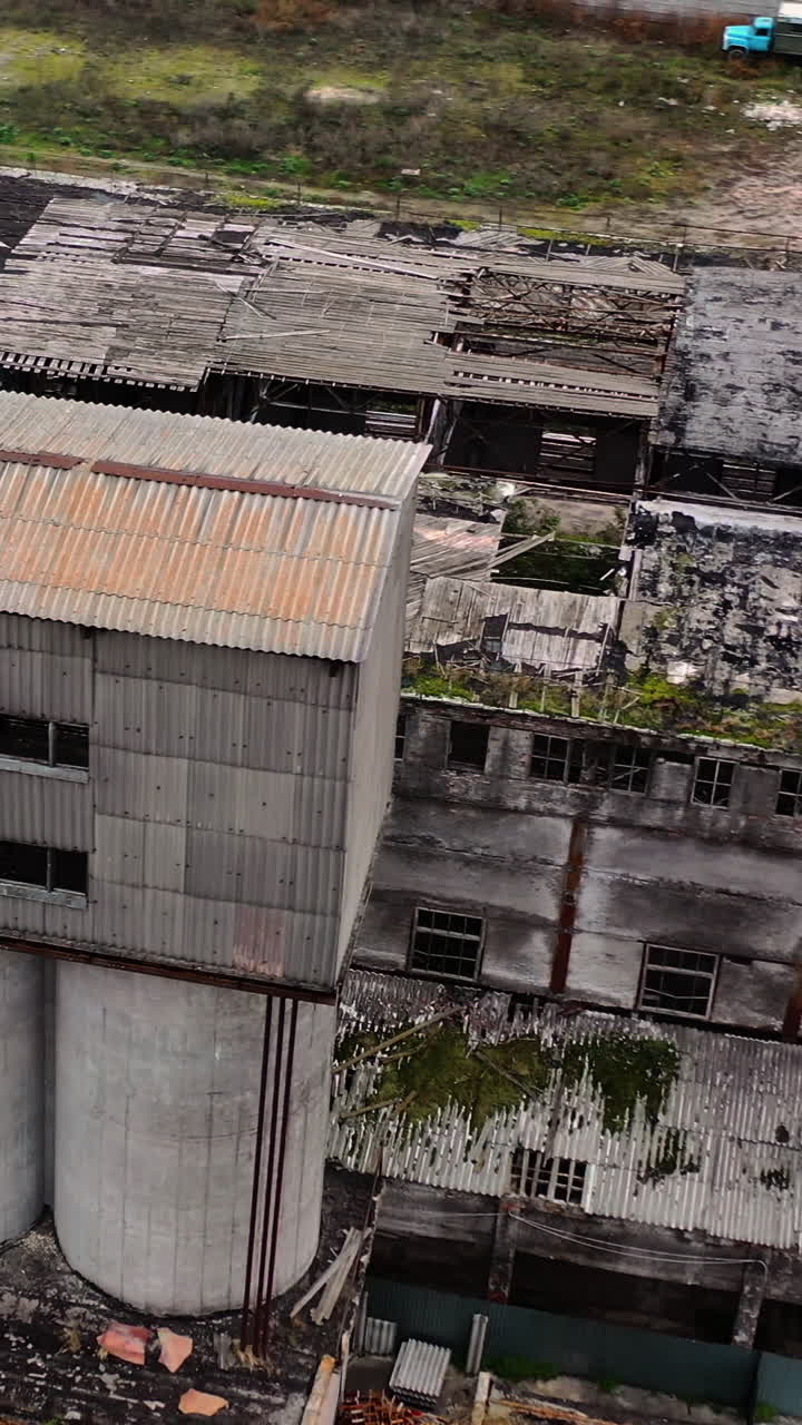Old abandoned plant. Damaged buildings on the field. Broken windows and roof of a ruined factory. Damaged industry. Aerial view. Vertical video