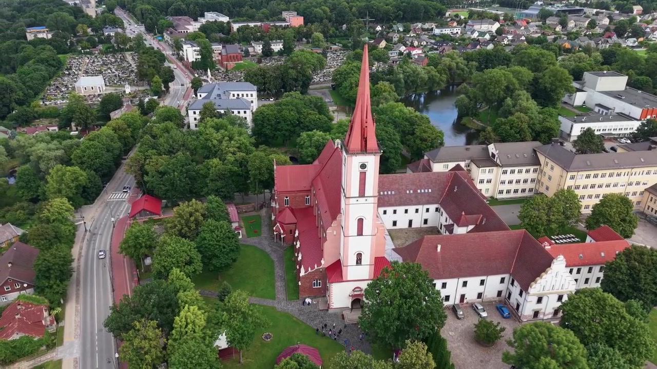 Splendide riprese aeree della Chiesa della Rivelazione del Signore alla Vergine Maria a Kretinga, Lituania, con tetti rossi, vegetazione lussureggiante, dintorni urbani e luce diurna chiara. Nessuna persona visibile