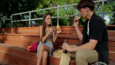 teenagers eating pizza and drinking soda in a park