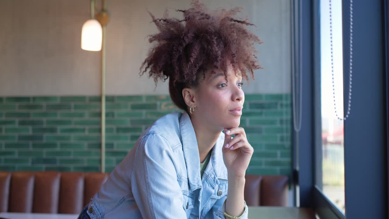 Window light guiding African American woman in denim jacket leaning, gazing then smiling at camera