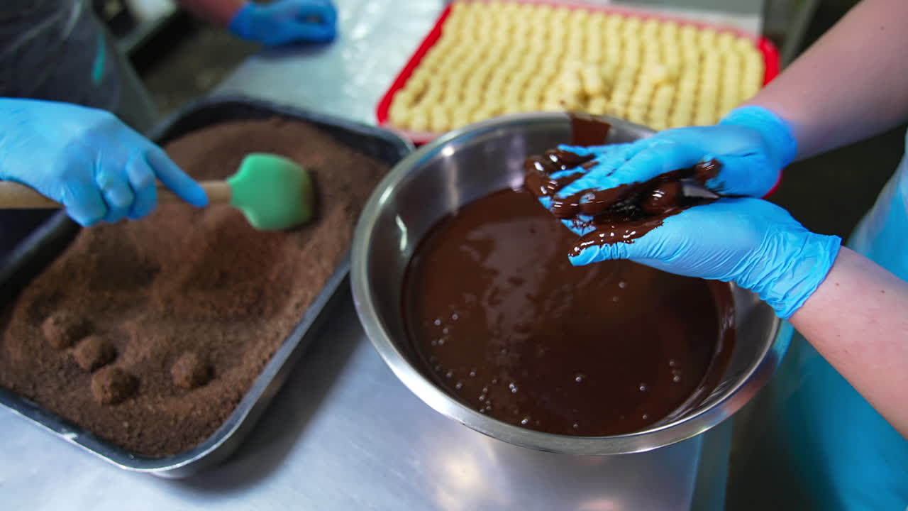 Producing handmade chocolate sweets. Two confectioners cover round sweets with chocolate and cocoa. Close up. Blurred background.