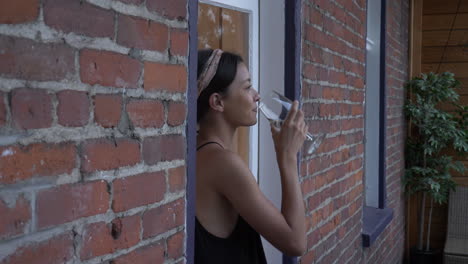 una joven feliz se sienta en la repisa de la ventana de un balcón bebiendo vino