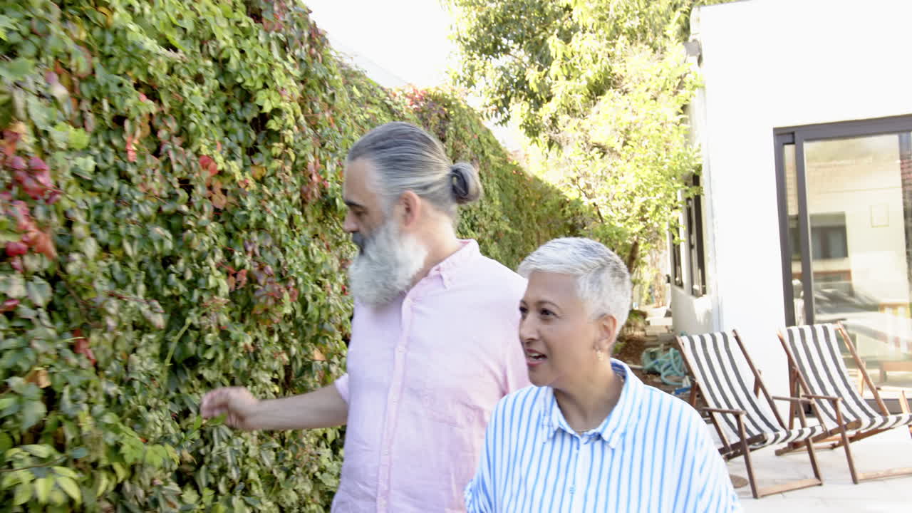 Senior couple walking and discussing plants in garden, enjoying nature together, copy space
