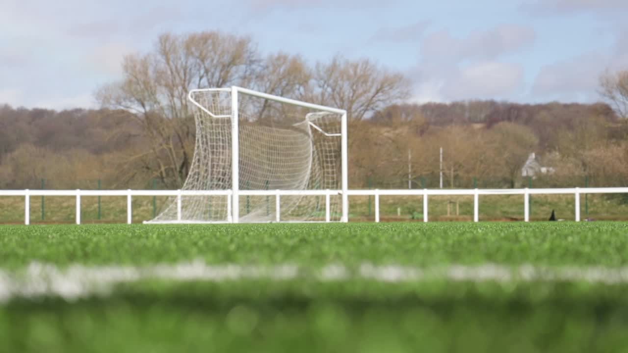 Low shot pulling focus from grass on a football pitch to a football goal net blowing in the wind
