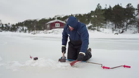 El-Hombre,-Acompañado-Por-Su-Perro,-Está-Empleando-Un-Hacha-Para-Hacer-Un-Agujero-En-El-Lago-Congelado-Para-Pescar-En-El-Hielo-En-Bessaker,-Condado-De-Trondelag,-Noruega---Toma-Estática