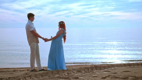 couple holding hands on sea beach at sunrise. pregnant couple beach