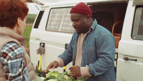 young women buying fresh vegetables from african american farmer