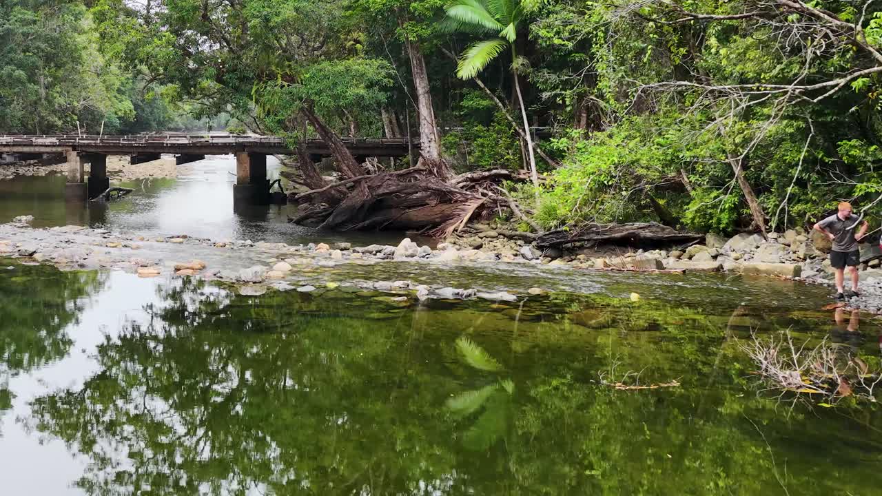 A serene creek in Port Douglas with a bridge and tourists exploring the lush rainforest environment