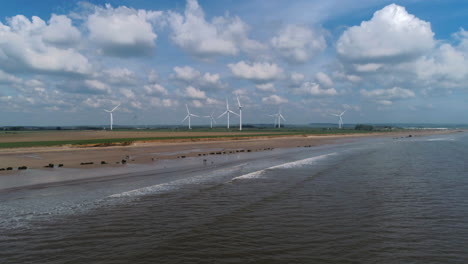 low establishing rising aerial drone shot rising over beach with fields of wind turbines on east coast of uk