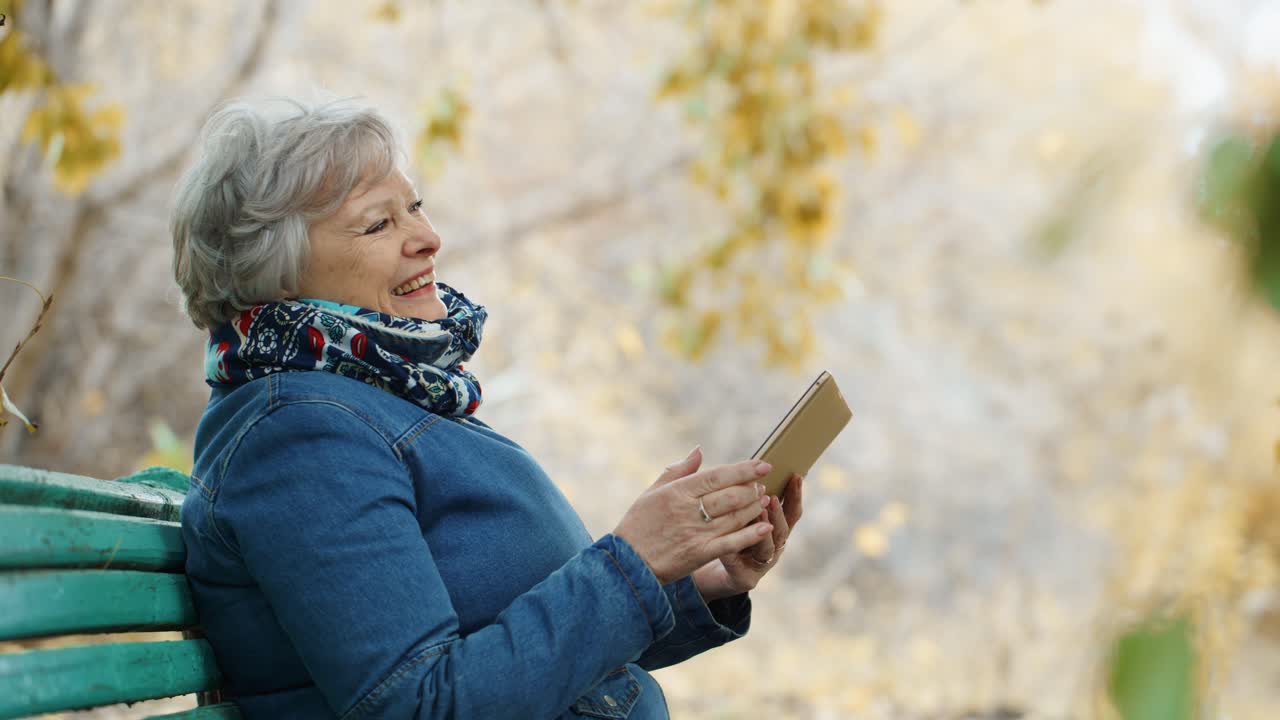 Senior Woman Using Tablet in Autumn Park