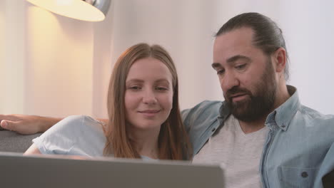 una pareja feliz tiene una conversación relajada sentada en el sofá y mirando la computadora portátil 2