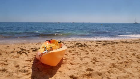 toma en cámara lenta de olas rompiendo en una cálida y soleada playa de arena detrás de un moderno kayak abierto amarillo