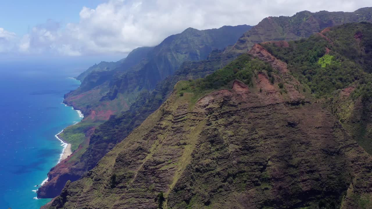 Ripresa fluida, in parallasse, 4K con drone delle creste della costa Na Pali dal sentiero Awa'awapuhi nel Waimea Canyon State Park a Kauai. Si vedono le nuvole bianche e gonfie, le creste verdi e lussureggianti e l'acqua turchese sottostante