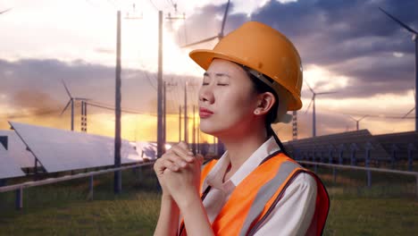 close up side view of asian female engineer with safety helmet pray for something with solar panel and wind turbines