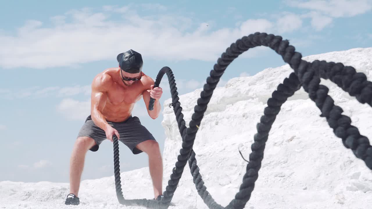 Muscular male athlete doing exercises with ropes. Workout on the nature against the sky with clouds