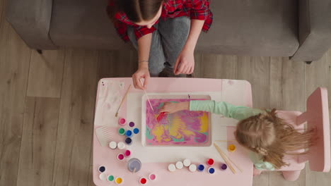 girl mixes paints with comb making ebru design with sister