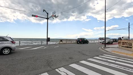 vehicles move through a seaside intersection in kamakura, japan. bright daylight and ocean backdrop create a serene urban scene