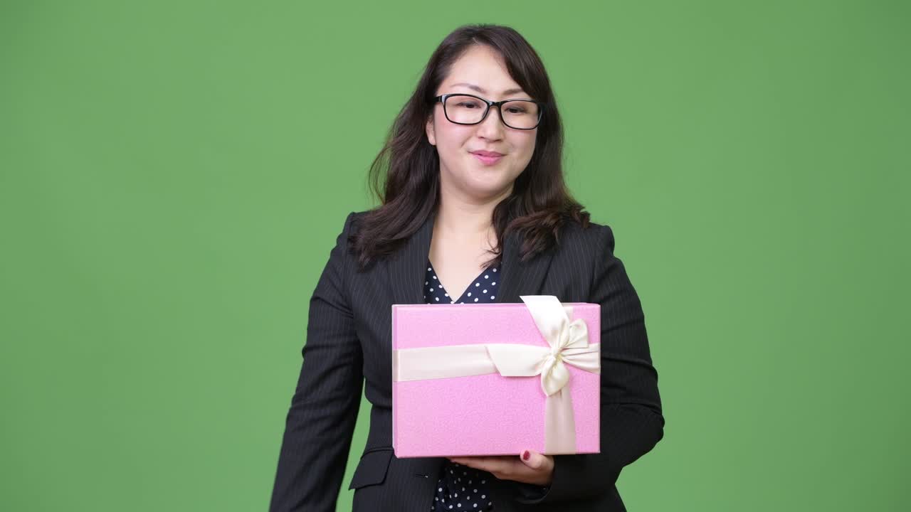Mature beautiful Asian businesswoman holding gift box and pointing to camera