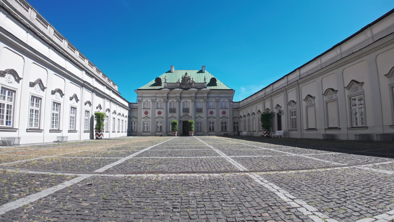 A sunny view of the Pałac Pod Blachą with cobblestone courtyard and clear sky