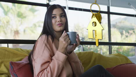 animation of gold house key and key fob over diverse woman dinking tea at home