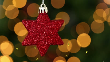 Animation-of-gold-confetti-falling-over-red-star-christmas-tree-decoration,-with-bokeh-lights-behind