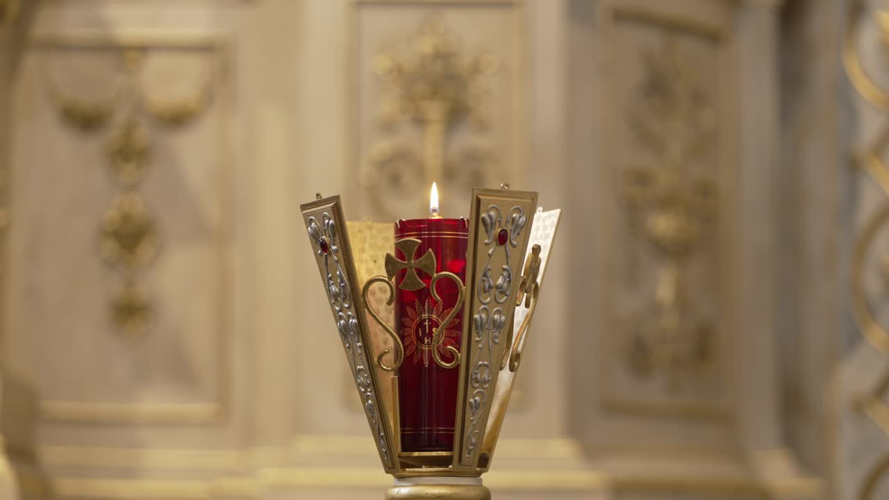 candelabro rojo adornado con una vela encendida, colocado contra un altar de la iglesia intrincadamente decorado