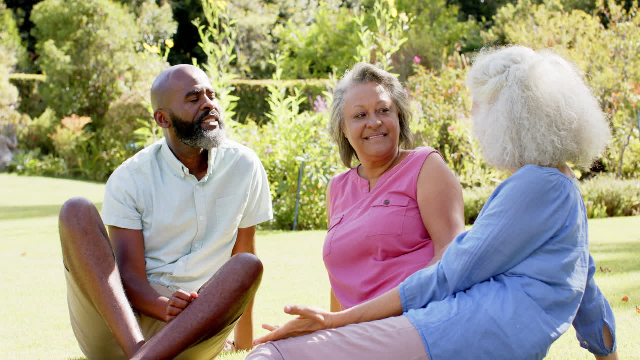 Enjoying outdoor conversation, senior friends sitting on grass in park
