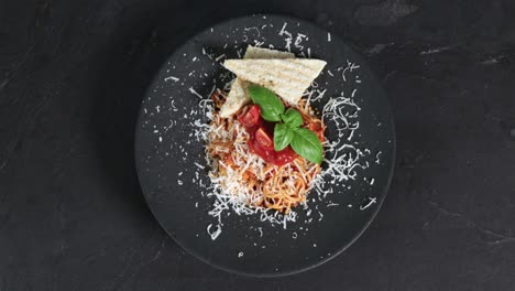 spaghetti bolognese with cheese garnished with bread, tomatoes and basil are presented on a rotating plate