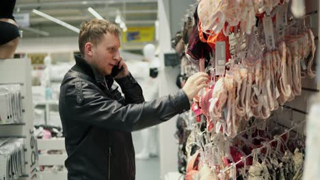 young man chooses a bra in lingerie store and talks on the phone