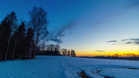 dramatic clouds flying at dawn in the morning with orange colored sunrise lighting over snowy winter field