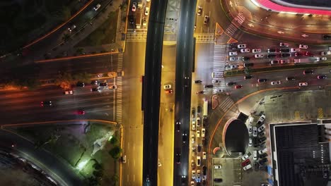 Night-traffic-at-city-intersection-with-highway-bridge-overpass,-aerial-overhead