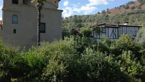ascending flight seeing garden vegetation and then the sanctuary appears on one side and on the other a large white house with wood on the façade called the santero's house, we see the surroundings