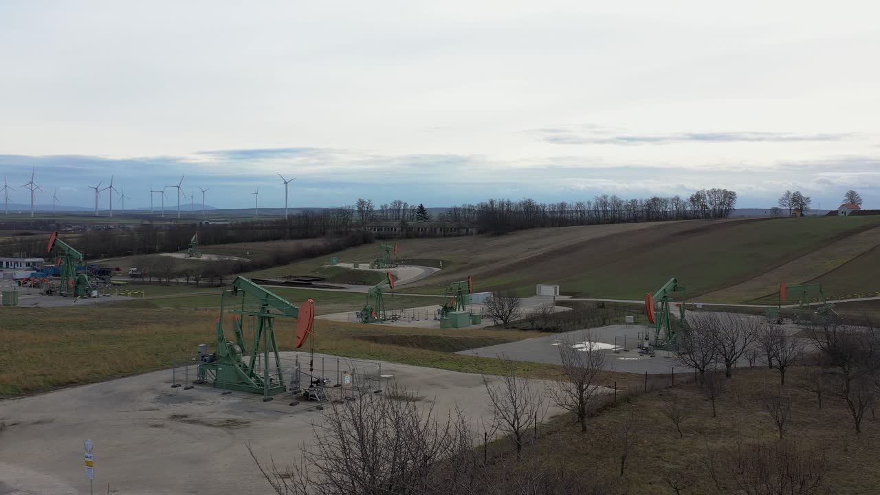 [drone]устойчивый снимок движущейся зелено-оранжевой нефтяной вышки с другими нефтяными вышками на заднем плане