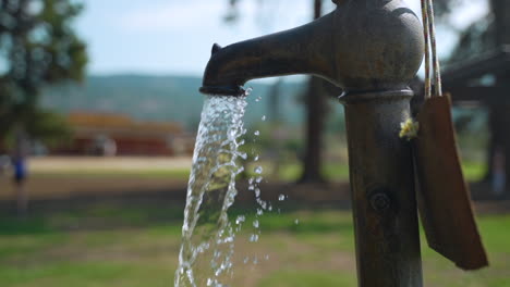 water comes pouring out of an old, vintage faucet in an outdoor park on a summer day