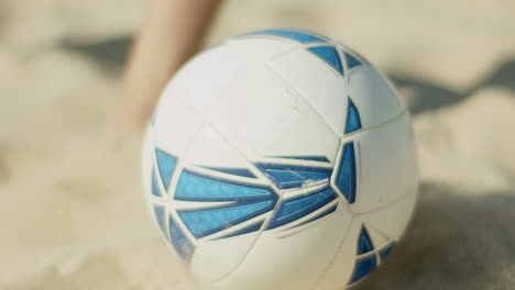 close-up shot of ball on sea shore hitting by boys leg