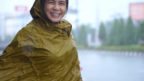 young cheerful woman in yellow wet raincoat jump and dancing on footpath next to main road with cars moving, having fun among heavy rain on raining day, funny girl dancing, living in rainy season