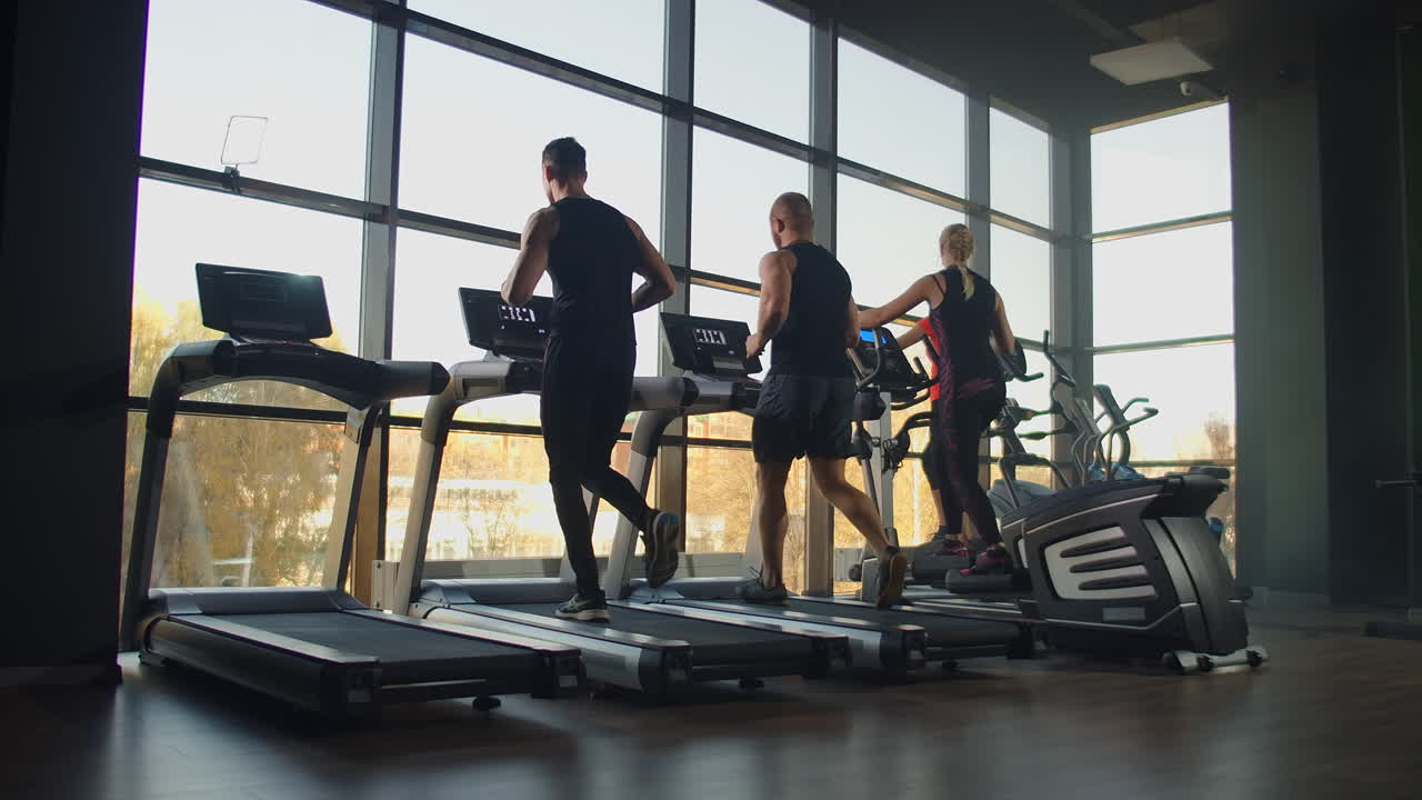 A group of people running on a treadmill in a fitness room performing a cardio workout. Men and women train together Running indoors warm-up before training in slow motion.