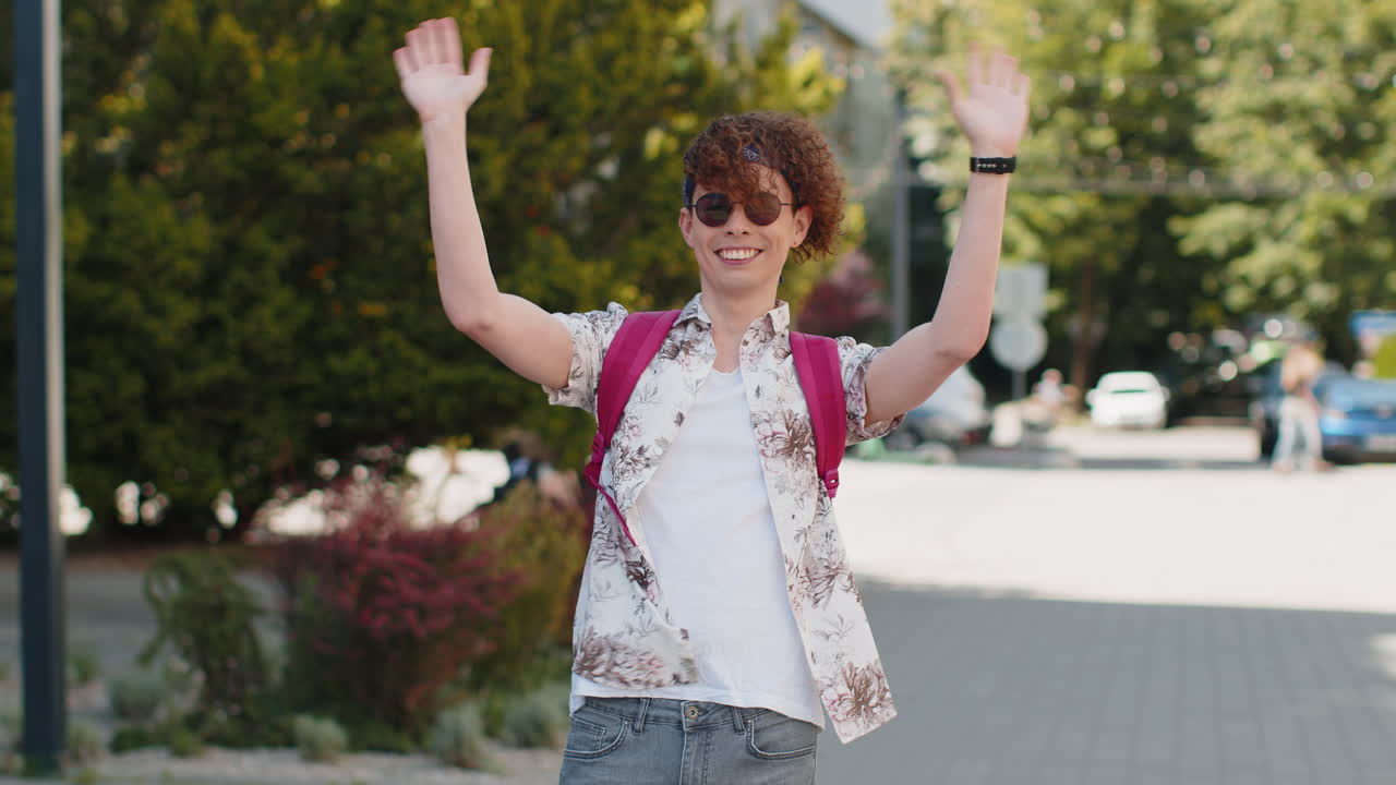 관광객이 카메라를 향해 우호적으로 미소 짓고 손을 흔들며 손짓을 하며 초대합니다. 안하세요.