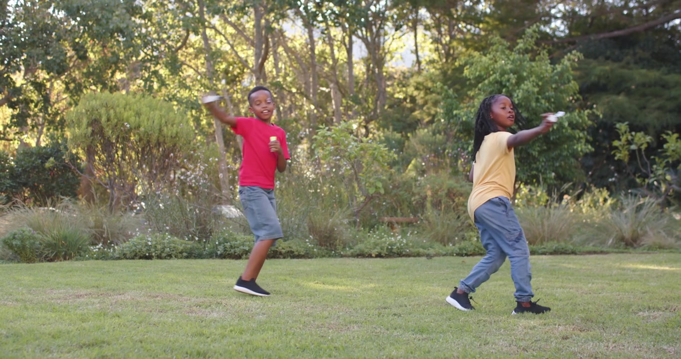 African American youth boys red shirt lifting wand, starting bubbles, playing on lawn with bottles