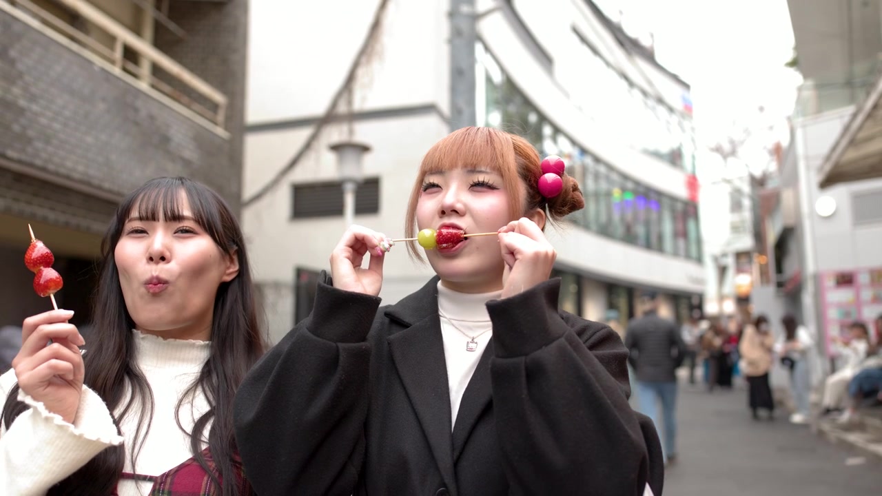 Due donne asiatiche gustano il cibo di strada tanghulu alle fragole mentre passeggiano per un quartiere dello shopping di Tokyo.