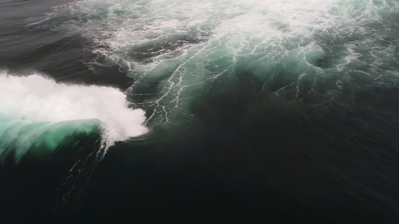 Slow motion wave forms smooth arc before crashing under overcast skies