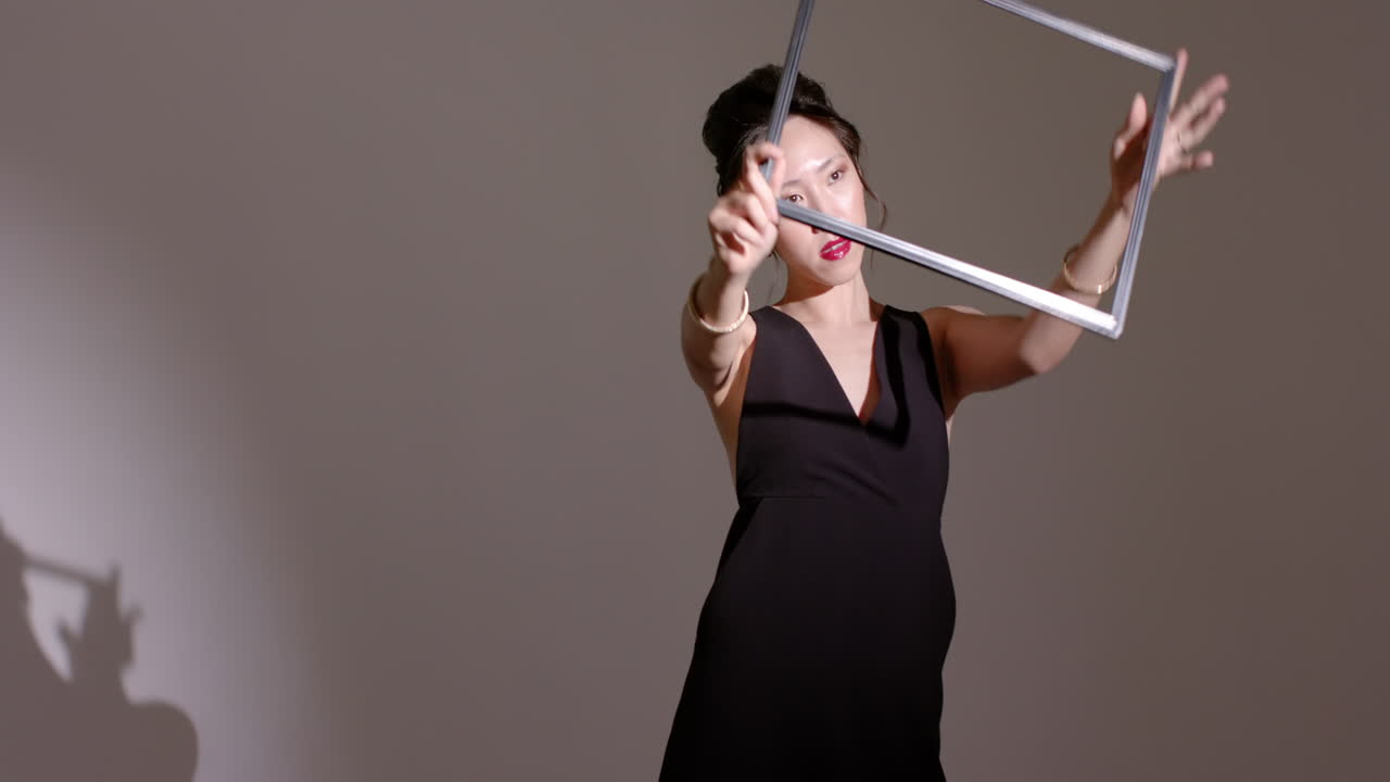 Chinese woman in black dress responding to spotlight casting frame shadow, rotating frame in studio