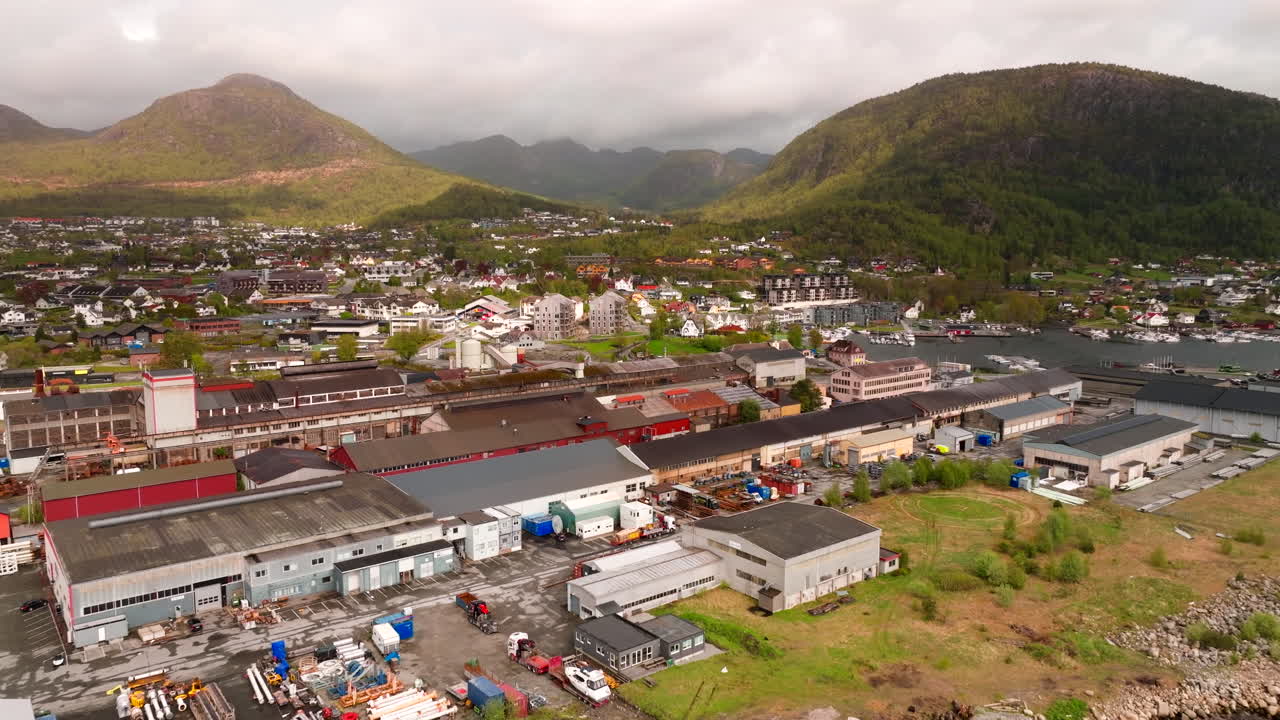 Drone pullback above steel mill facility by water near Jorpeland, Norway with smokestack and coast