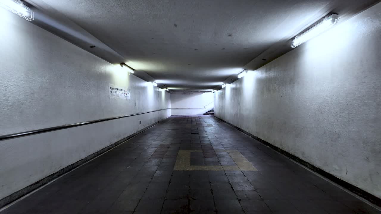 POV along deserted underpass tunnel featuring dim lighting and a vanishing perspective.