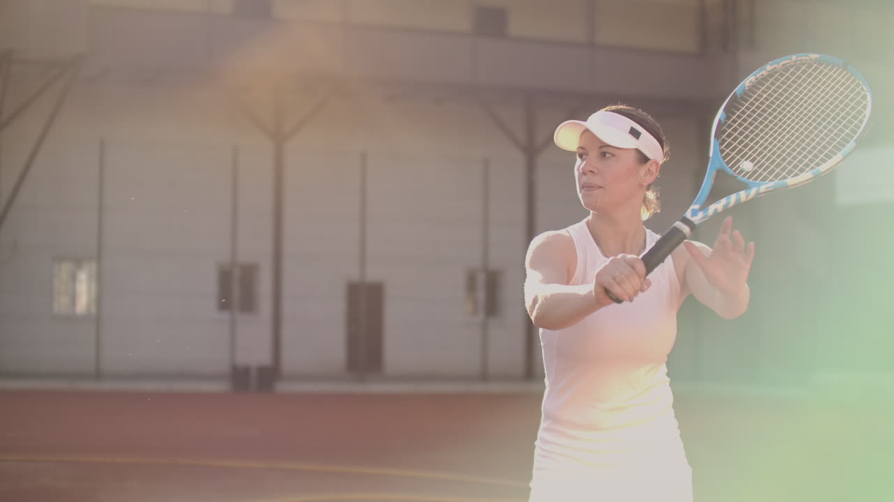 색 한 슈트를 입은 전문적인 여성이 라켓으로 공을 때리고 테니스 코트에서 역동적으로 뛰고 있습니다.