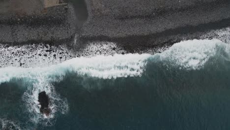 Vista-Aérea-De-Las-Olas-Rompiendo-En-Una-Playa-De-Guijarros,-Agua-Turquesa-Y-Espuma-Blanca.